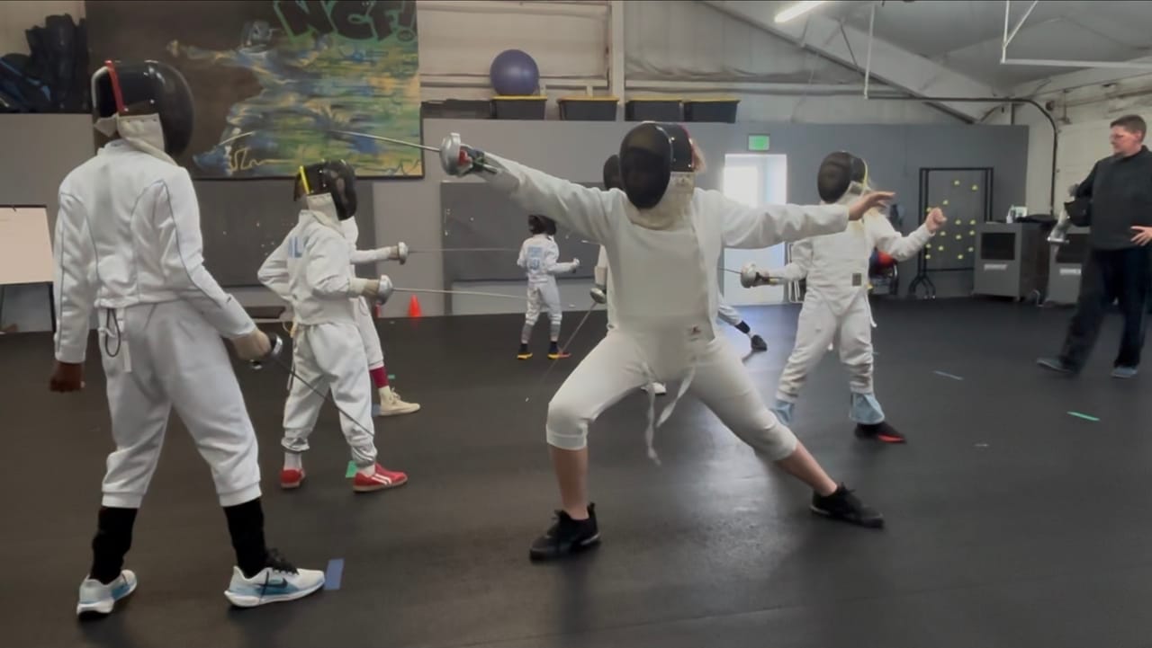 Young epee fencers in lunge and en-garde positions during a coached group session at NCF Boulder